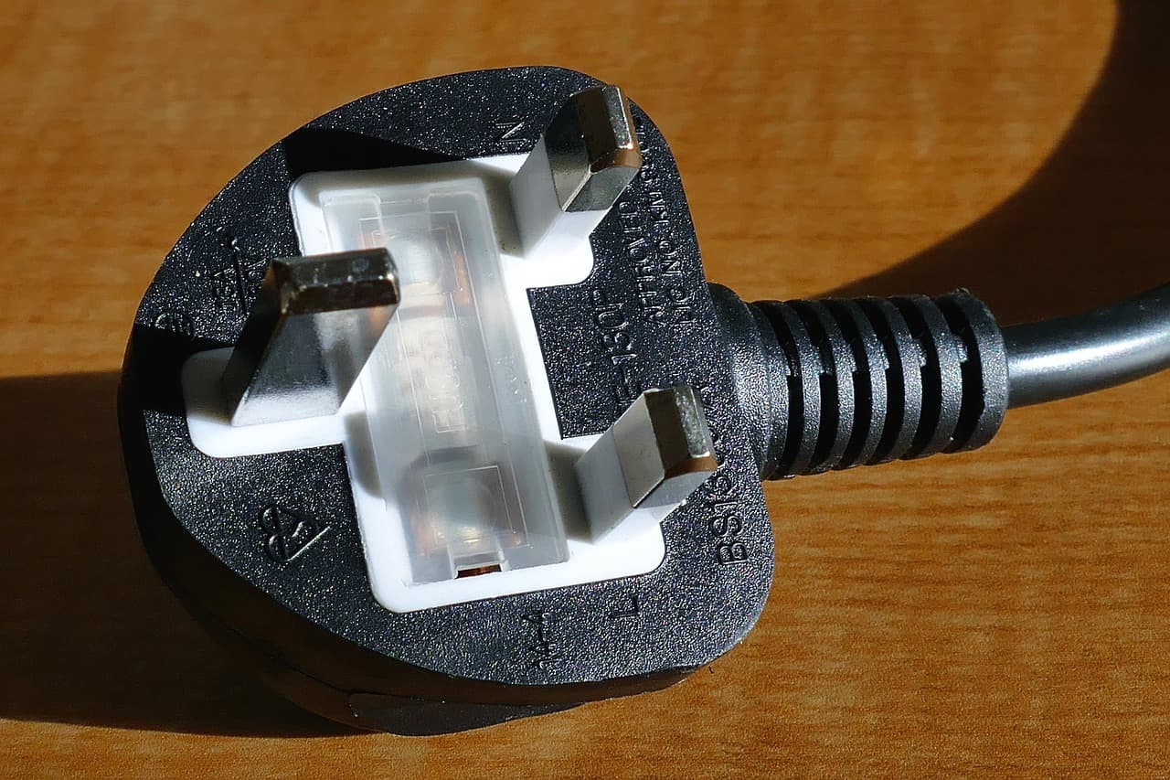A UK three-pin plug with its cable, on a wooden floor