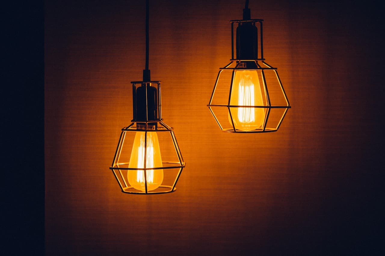 Two caged filament pendant lights glowing against a dark wall