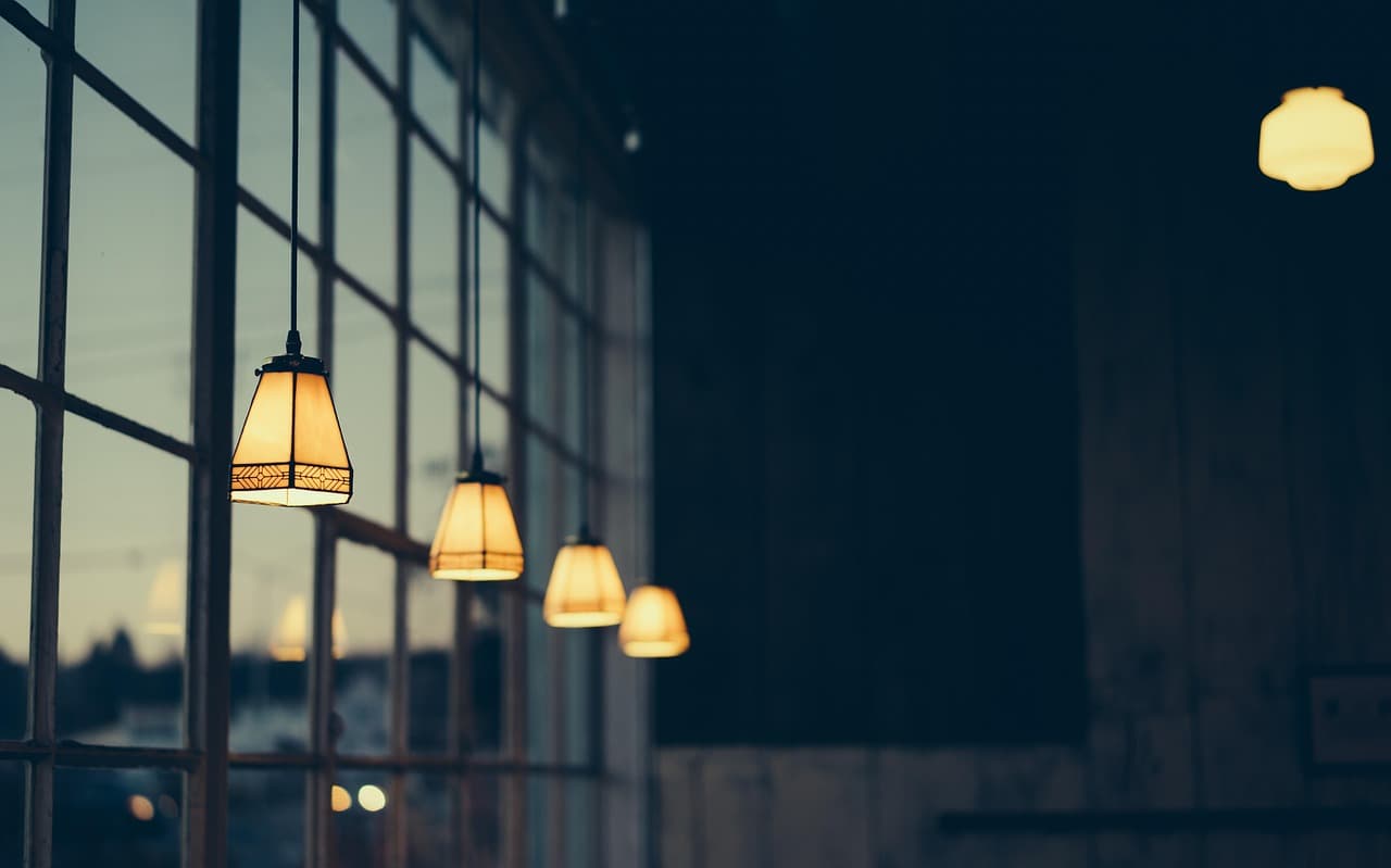 A row of glowing pendant lamps along a tall window at dusk